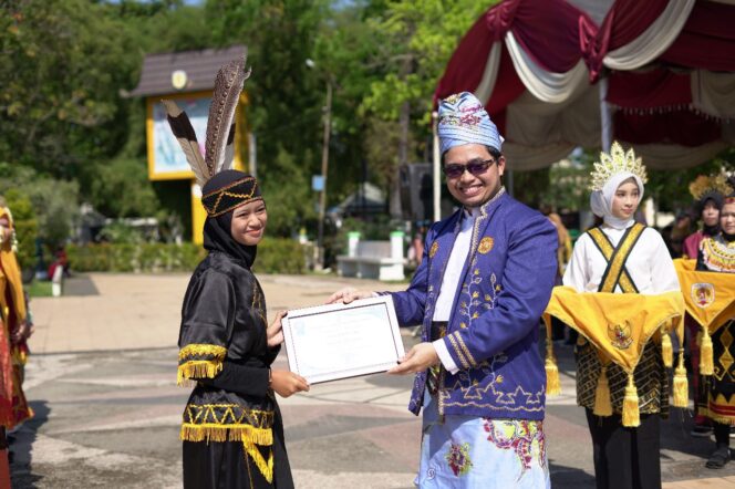 
 Bupati Aulia saat mengenakan pakaian khas Kesultanan Banjar menyerahkan piagam penghargaan kepada pelajar berprestasi usai Apel Hardiknas di Lapangan Dwi Warna Barabai, Kamis (25/5/2023).
